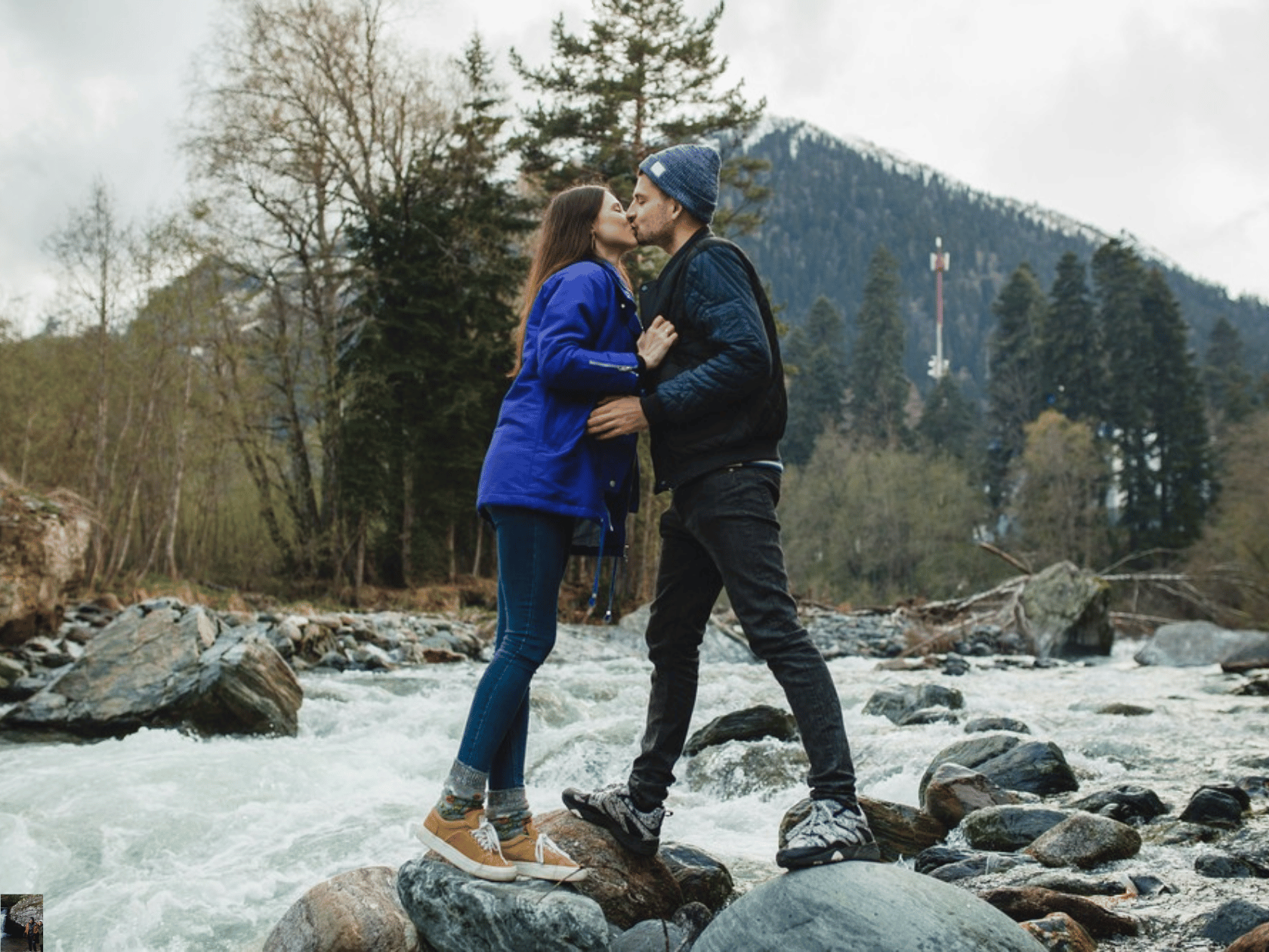 A couple standing over a calm river bed and kissing in the winter weather